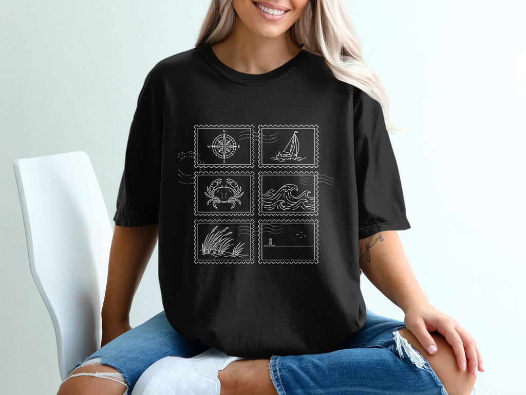 Black t-shirt with postage stamp designs of a compass, crab, waves, grass, and sailboat.