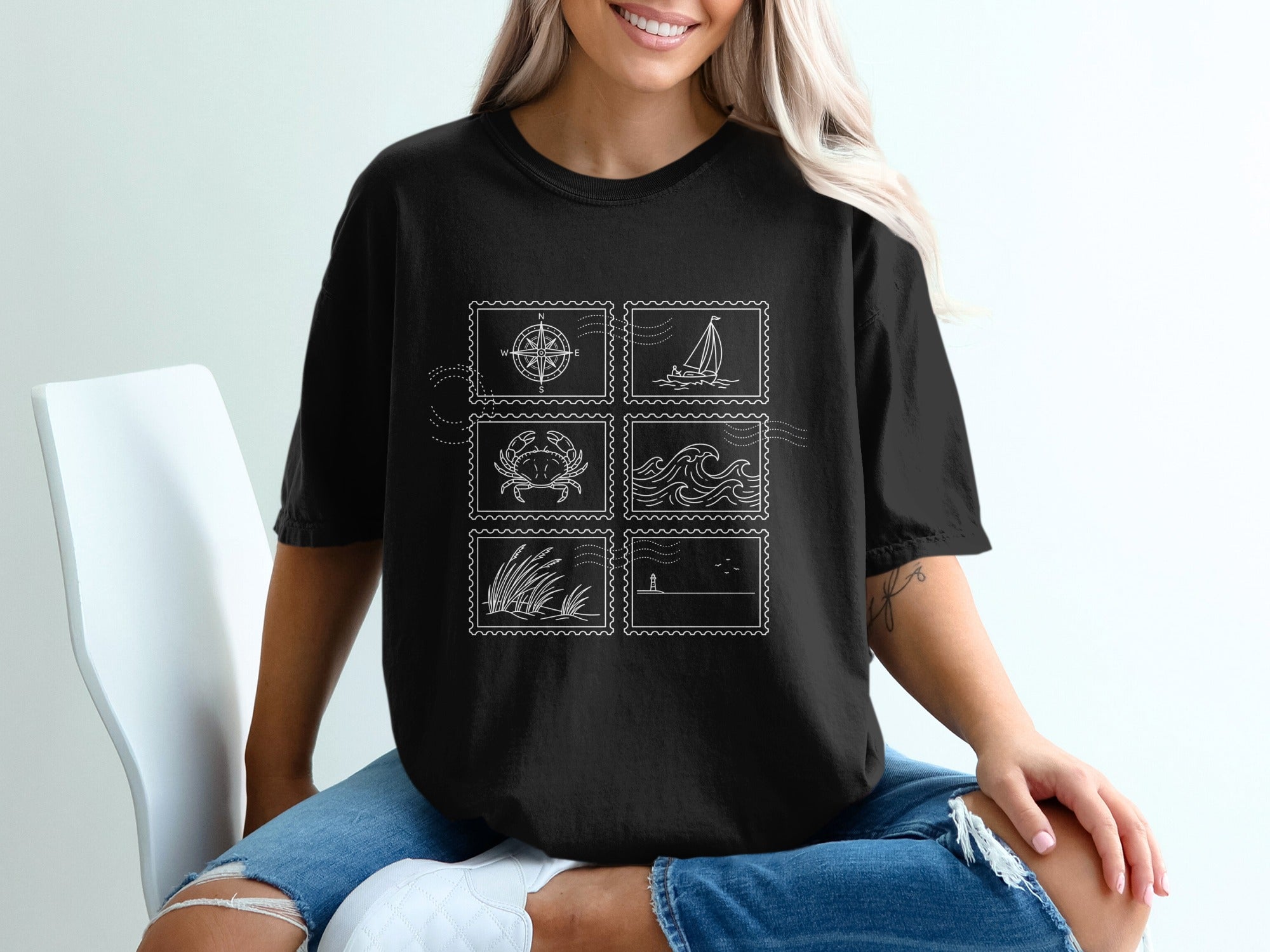 Black t-shirt with postage stamp designs of a compass, crab, waves, grass, and sailboat.