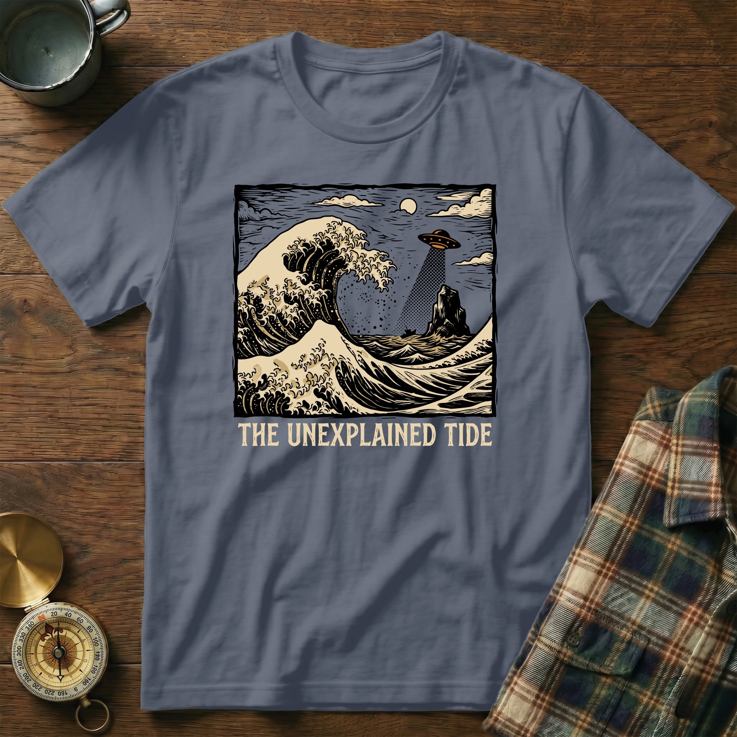T-shirt with "The Unexplained Tide" design featuring a crashing wave, UFO, and island.