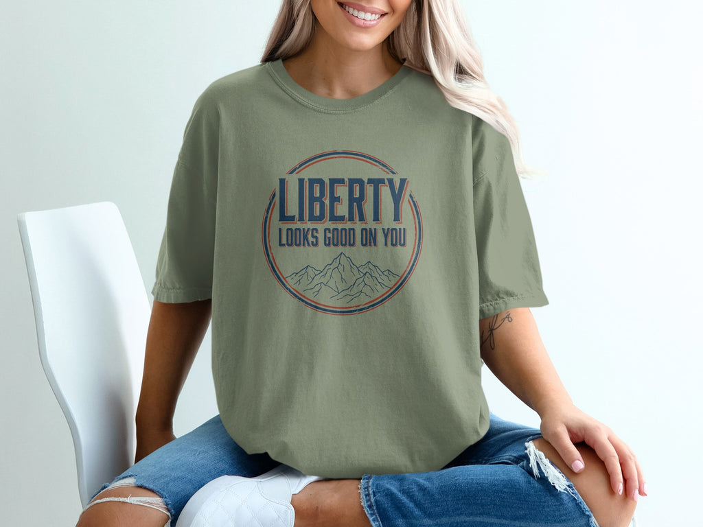 Olive t-shirt with "Liberty Looks Good On You" text and mountain graphic.