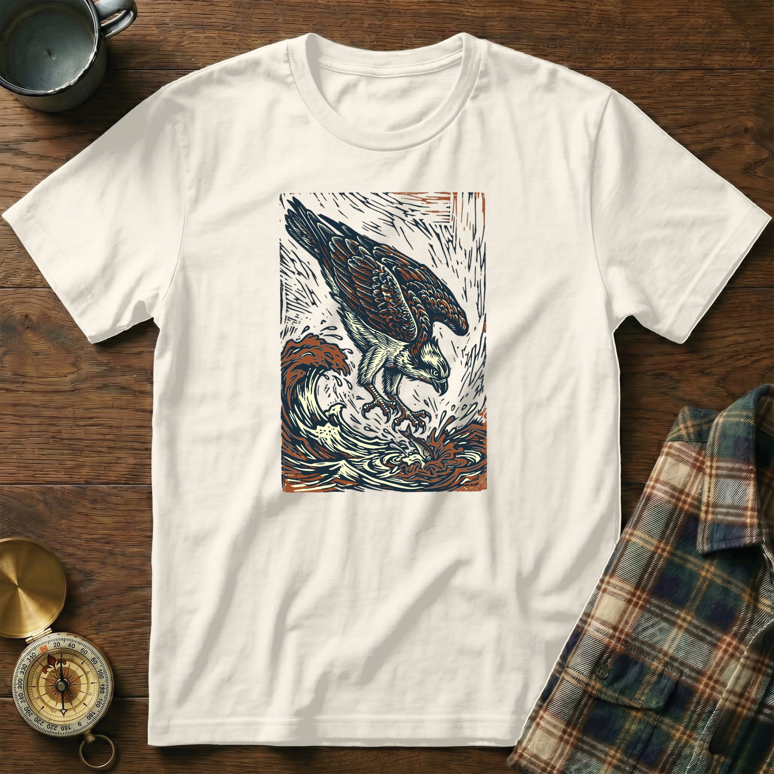 White t-shirt with woodgrain and plaid background, featuring an osprey diving into waves.