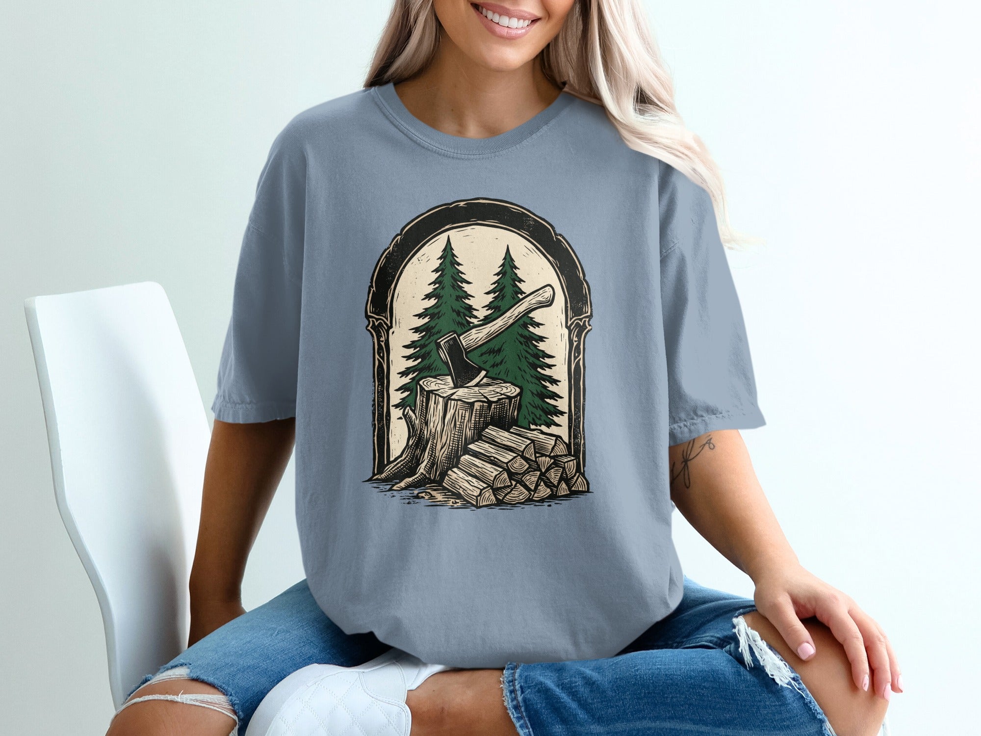 T-shirt graphic of axe in wood stump with pine trees and logs.
