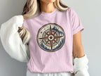 Pink t-shirt with a distressed compass graphic featuring mountains and pine trees.