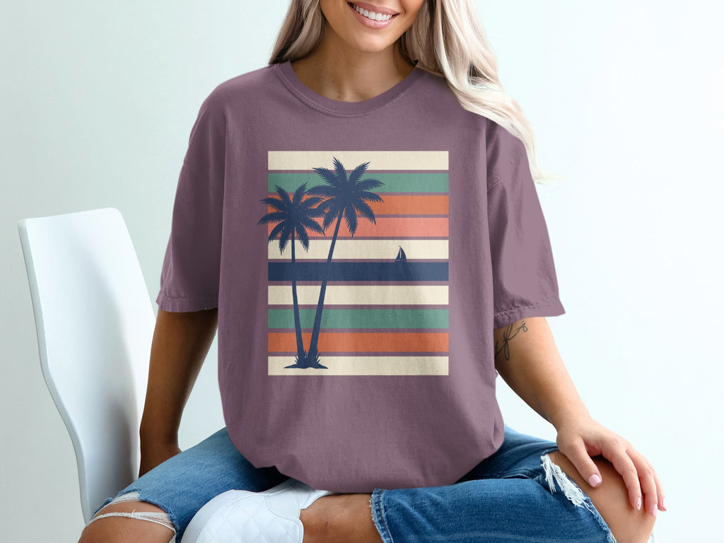 Purple t-shirt with silhouetted palm trees and sailboat on striped background.
