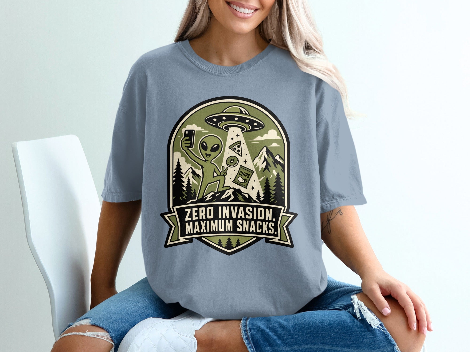 Graphic t-shirt with alien, UFO, and snacks, reads "Zero Invasion. Maximum Snacks."