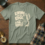 T-shirt with text "Living on the edge, barely" and a goat hanging from a cliff.