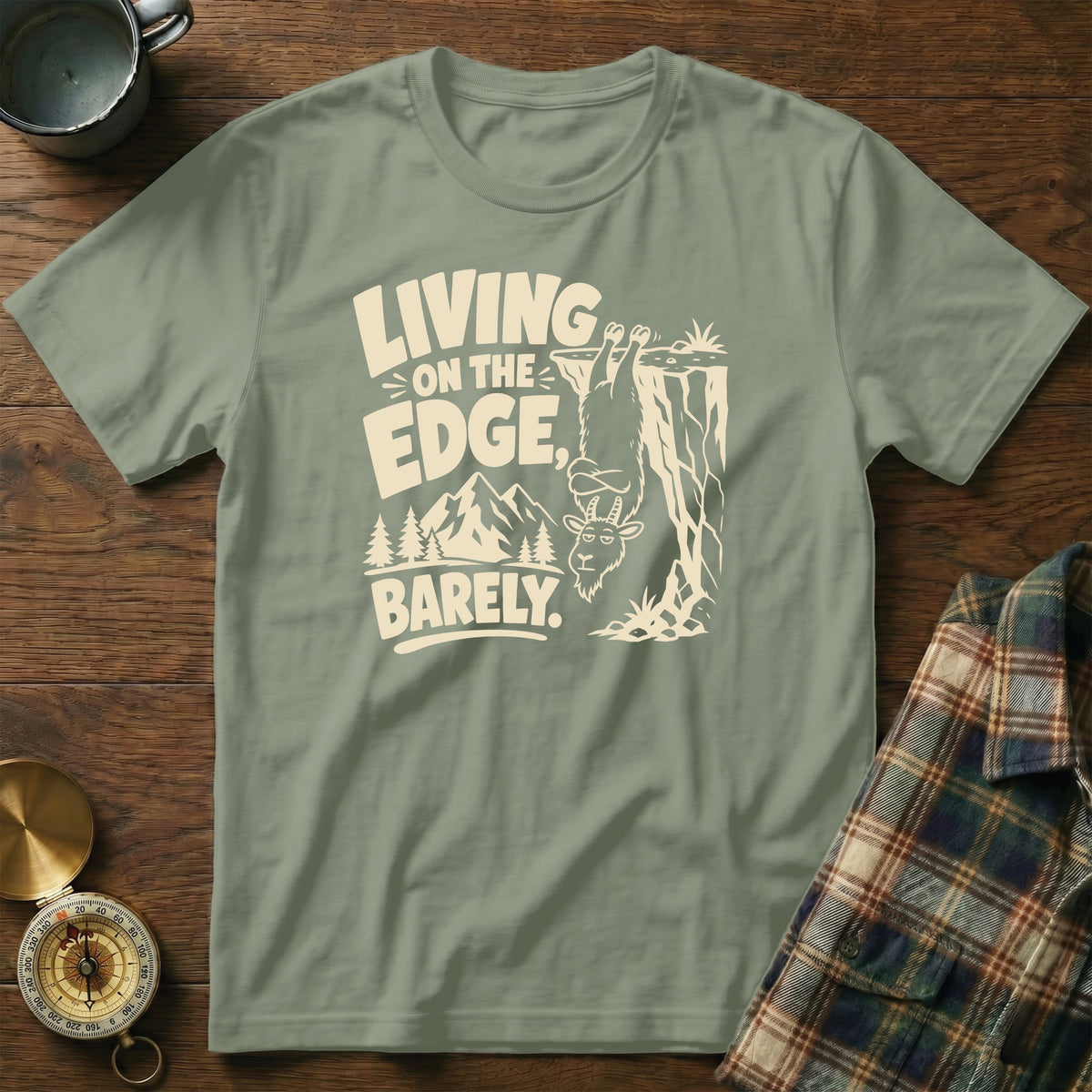 T-shirt with text "Living on the edge, barely" and a goat hanging from a cliff.