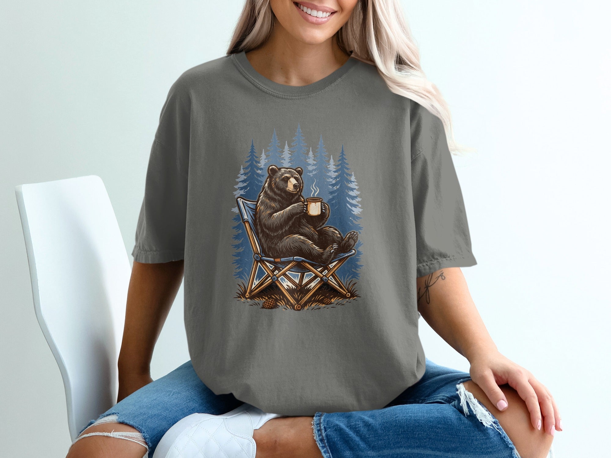 Bear sitting in a camping chair with a mug, in front of pine trees.