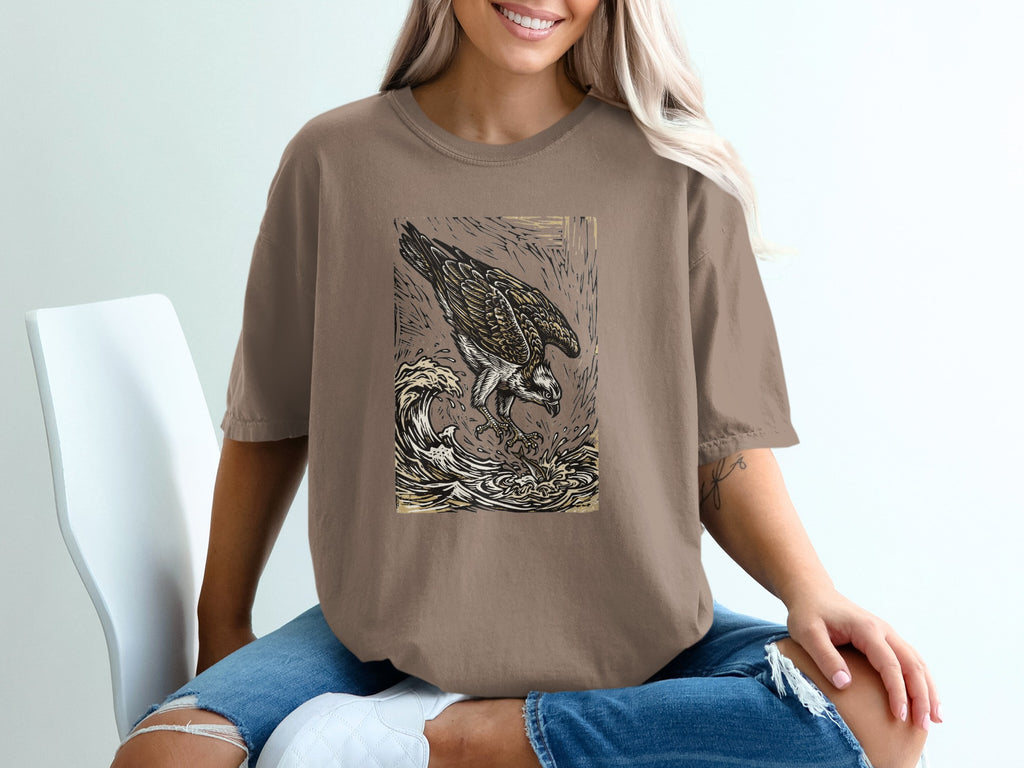 Brown t-shirt with graphic of an osprey diving for fish in choppy waves.