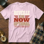 A light pink t-shirt printed with the text "REVELLE IS NOW OPTIONAL EFFECTIVE IMMEDIATELY" lies on a wooden surface beside a mug, a compass, and a plaid shirt.