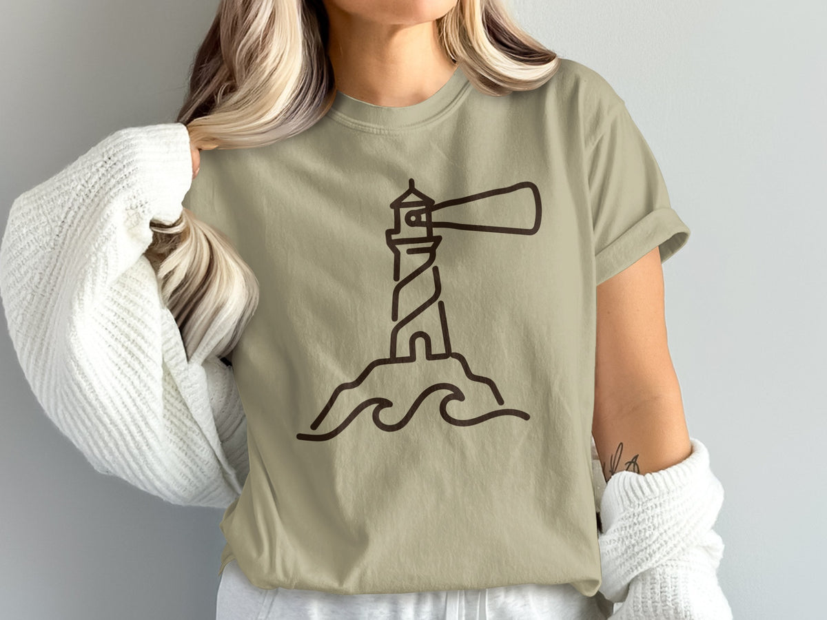 Tan t-shirt with a minimalist brown outline drawing of a lighthouse on a rock with waves.