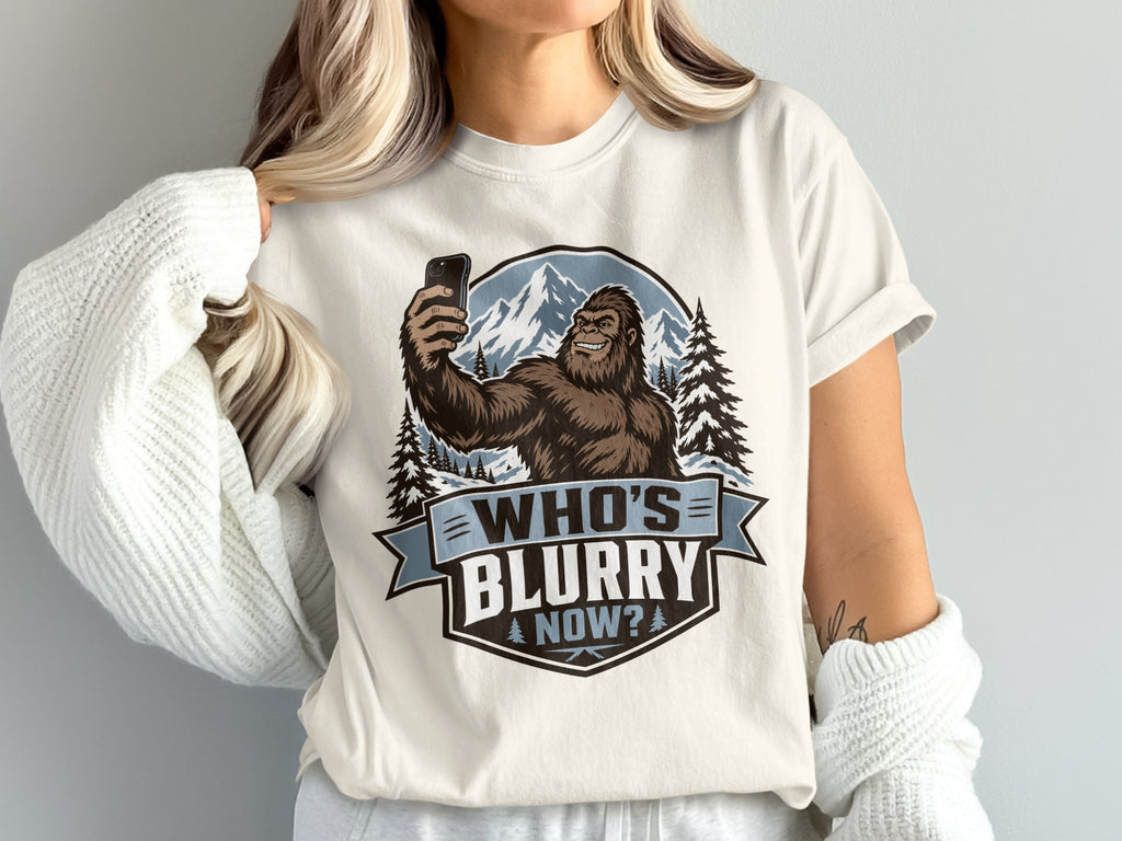 Bigfoot taking a selfie in front of mountains and trees, text reads "WHO'S BLURRY NOW?".