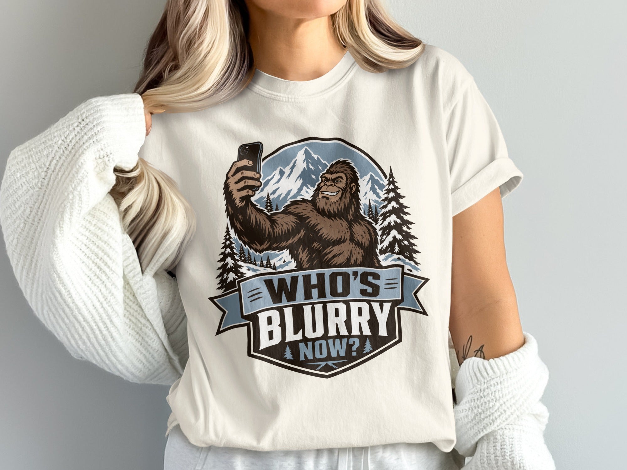 Bigfoot taking a selfie in front of mountains and trees, text reads "WHO'S BLURRY NOW?".