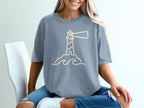 Grey t-shirt with a cream outline graphic of a lighthouse on rocks with waves.