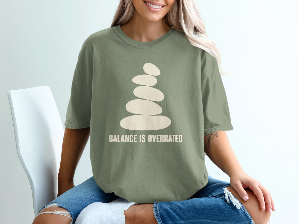 Olive green t-shirt with stacked stones graphic and text "BALANCE IS OVERRATED".
