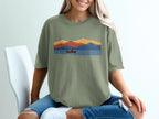 Green t-shirt with abstract mountain and lake graphic featuring a person kayaking.