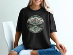 Black t-shirt with a circular mountain and forest scene reflected in water.