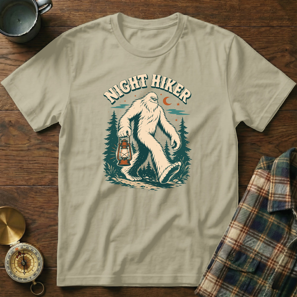 T-shirt with Bigfoot holding a lantern in a forest, text "NIGHT HIKER" above.