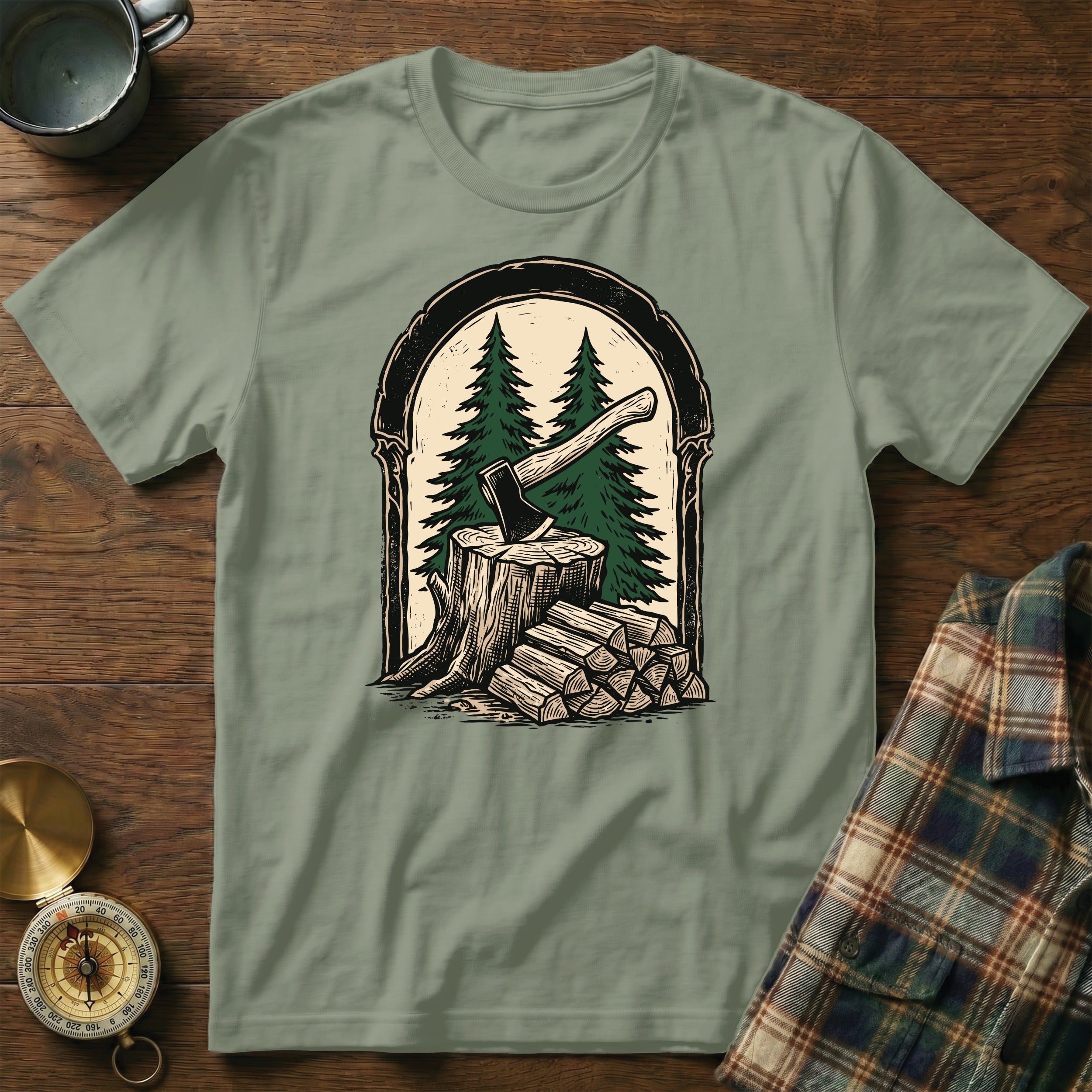 Green t-shirt with graphic of axe in wood stump, pine trees, and firewood.