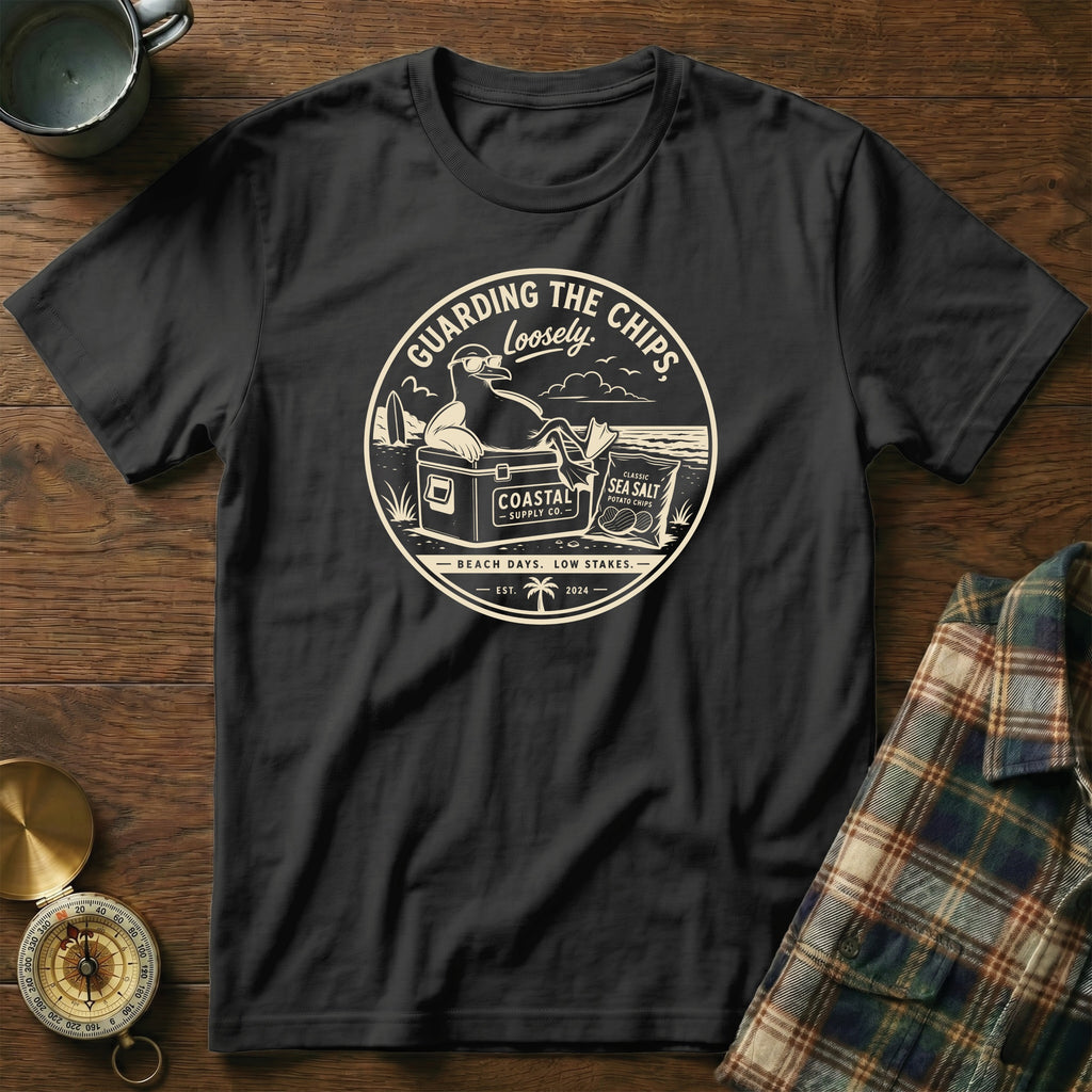 Black t-shirt with graphic of a seagull guarding potato chips on a beach.