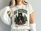 Graphic t-shirt with bear by campfire, tent, and text "GO OUTSIDE" and "GREAT VIEW. UNCLEAR EXIT."