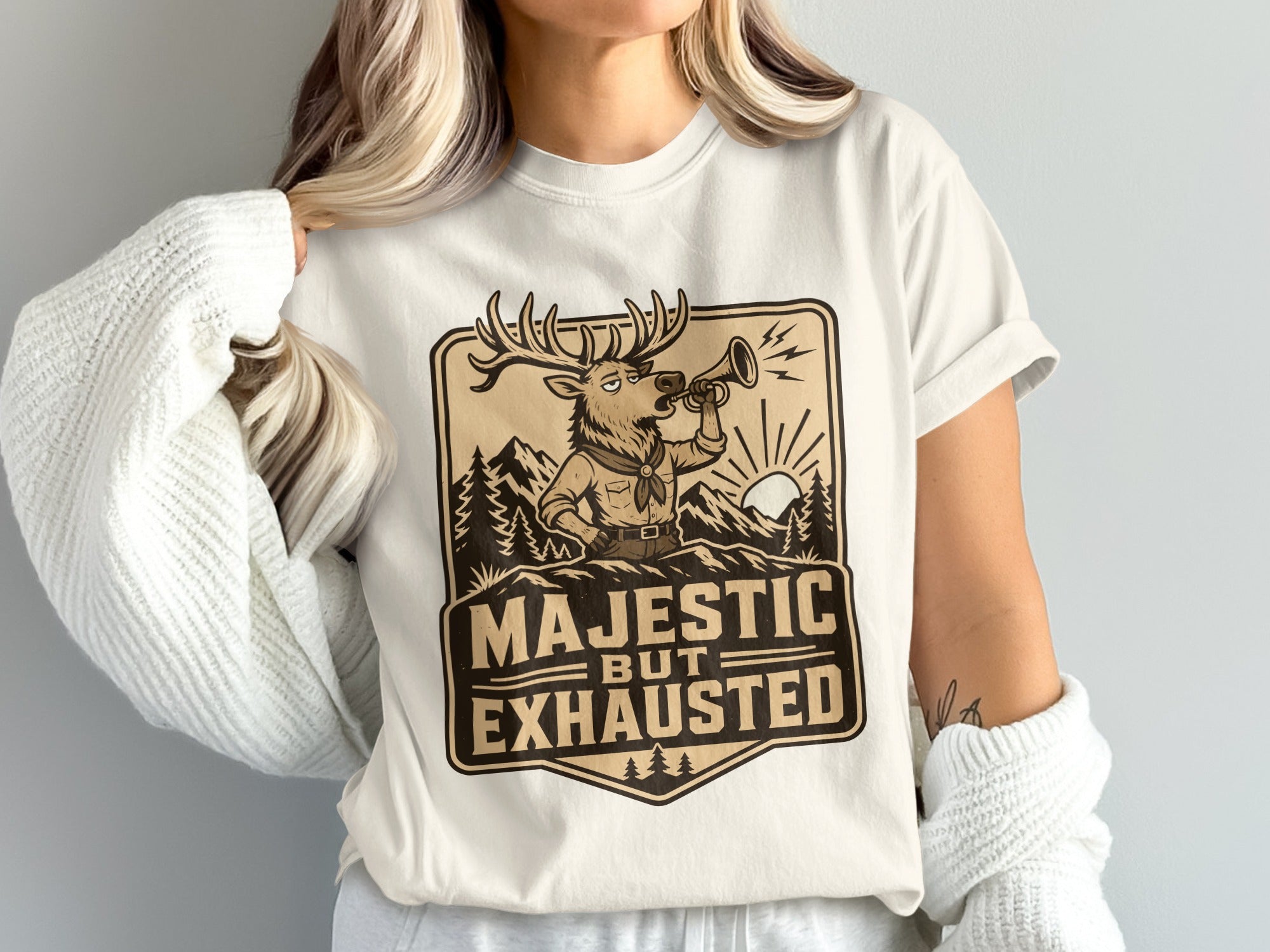 T-shirt graphic: deer blowing horn in mountains, text "Majestic But Exhausted."