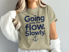 A woman wearing an olive-green t-shirt printed with dark blue text reading Going with the flow. Slowly. and an anchor graphic.