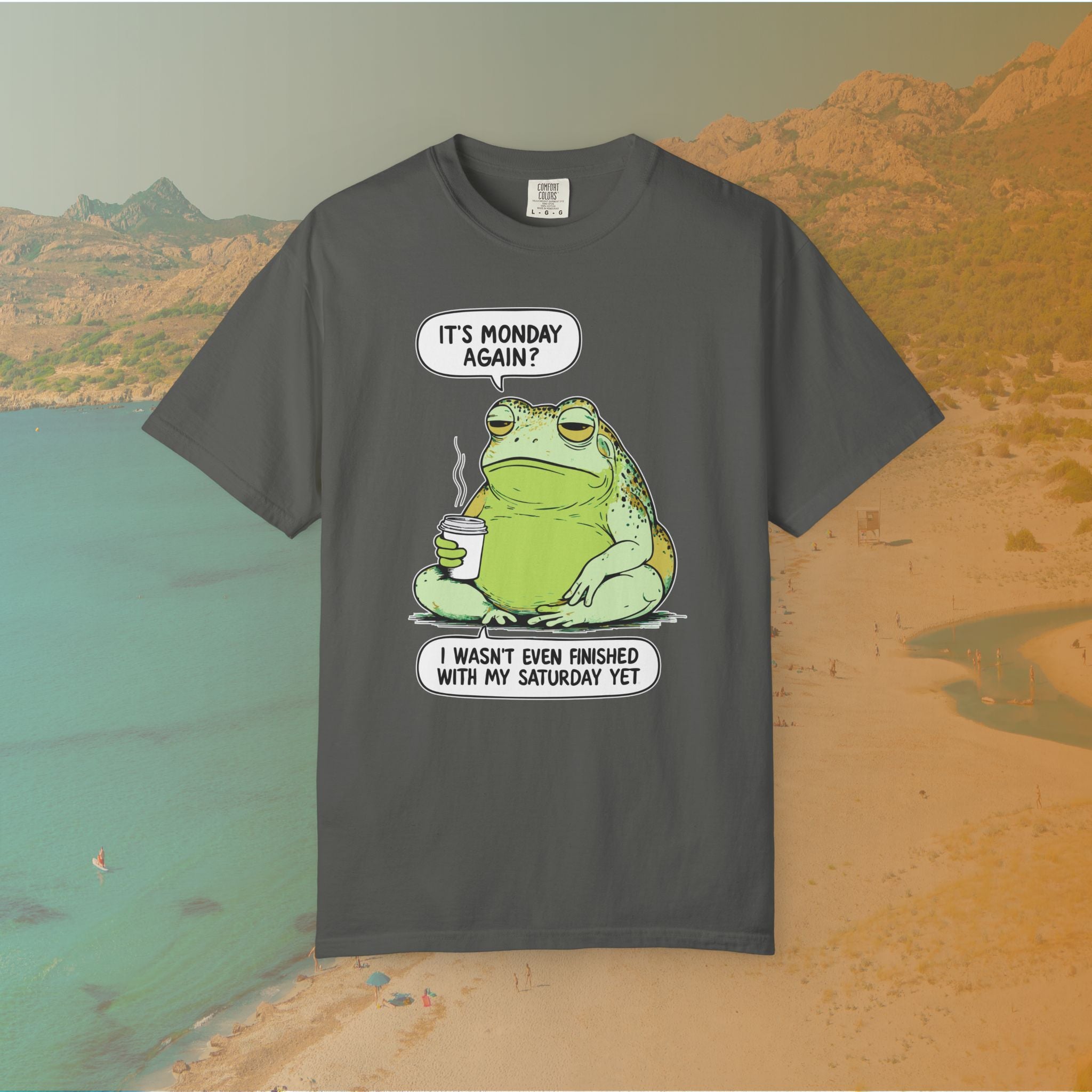 Funny T-shirt graphic featuring a large, grumpy toad holding a to-go coffee cup. The cartoon is captioned with the quotes: "IT'S MONDAY AGAIN? I WASN'T EVEN FINISHED WITH MY SATURDAY YET.