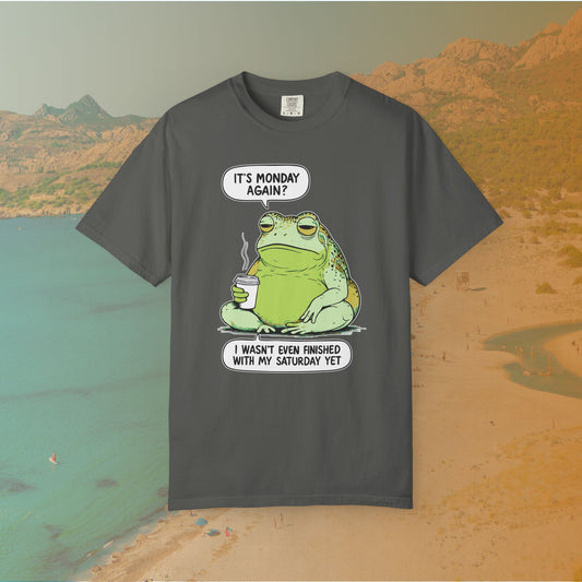 Funny T-shirt graphic featuring a large, grumpy toad holding a to-go coffee cup. The cartoon is captioned with the quotes: "IT'S MONDAY AGAIN? I WASN'T EVEN FINISHED WITH MY SATURDAY YET.