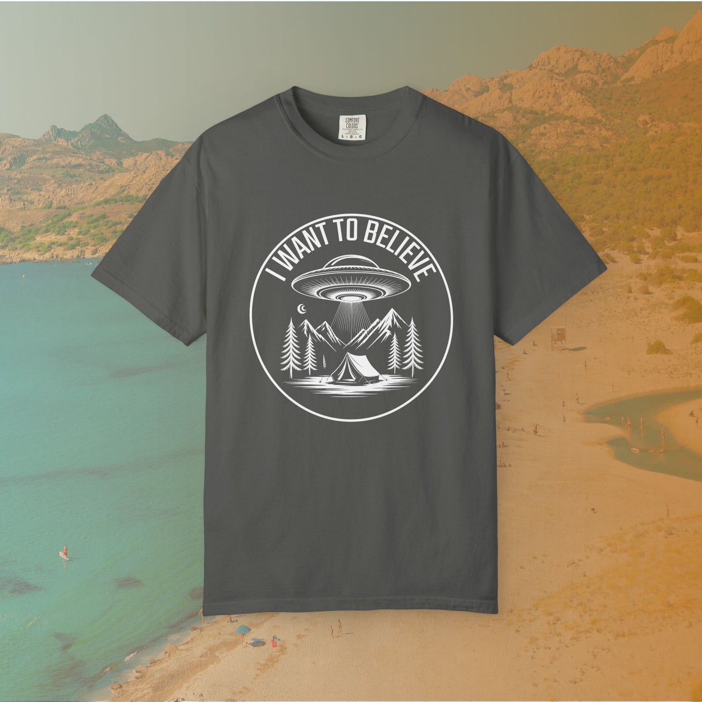 grey  t-shirt A round, white graphic on a dark background featuring a classic flying saucer UFO abducting a tent at a campsite surrounded by mountains and pine trees. The surrounding text reads "I WANT TO BELIEVE.
