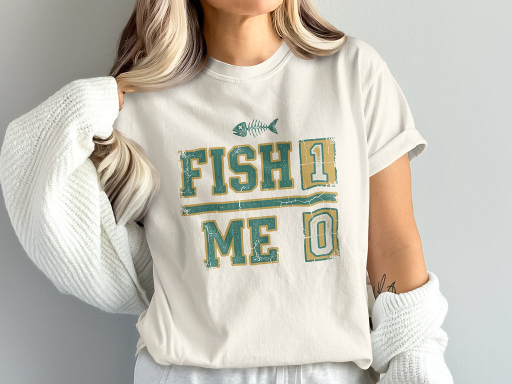 Cream t-shirt with "FISH 1 ME 0" text and fish skeleton graphic.