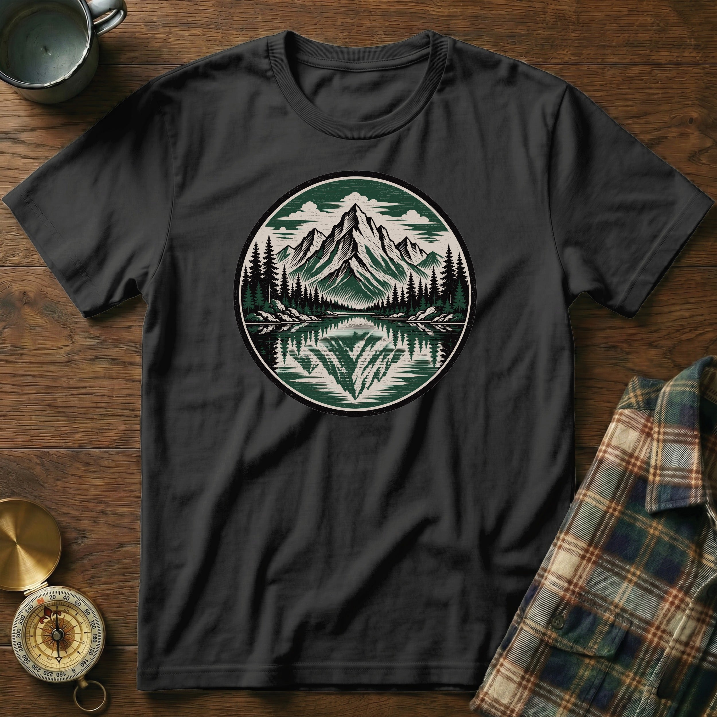 Black t-shirt with a circular mountain and lake graphic, compass, and folded plaid shirt.