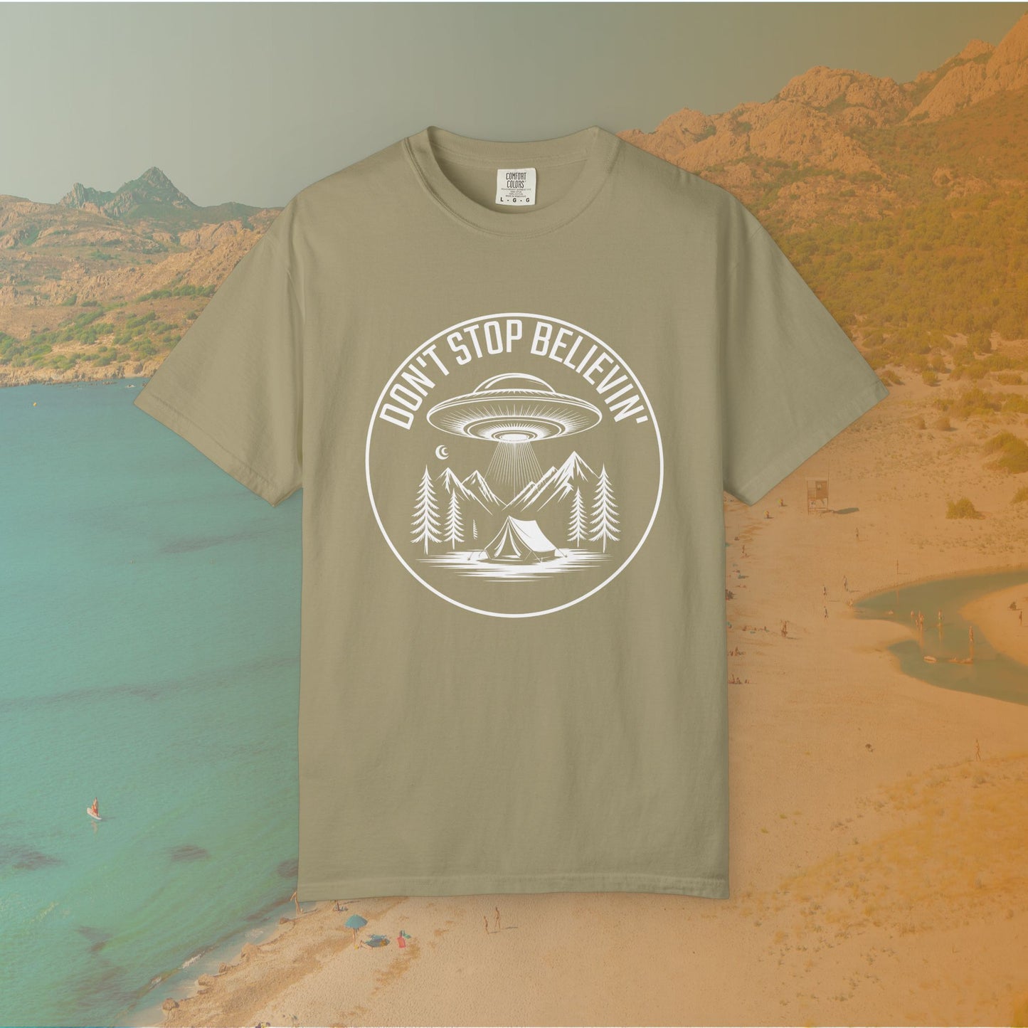 khaki t-shirt Keep believing, no matter what's out there! This awesome graphic tee features the famous rock slogan, DON'T STOP BELIEVIN', surrounding a detailed scene of a UFO hovering over a mountain campsite.