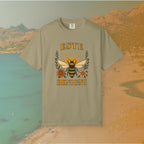 khaki t-shirt Vintage-style graphic tee featuring a large, central honey bee with sunburst wings, flanked by retro flowers. The Latin words "ESTE BENIGNI" for "BEE KIND" are printed above and below the design.