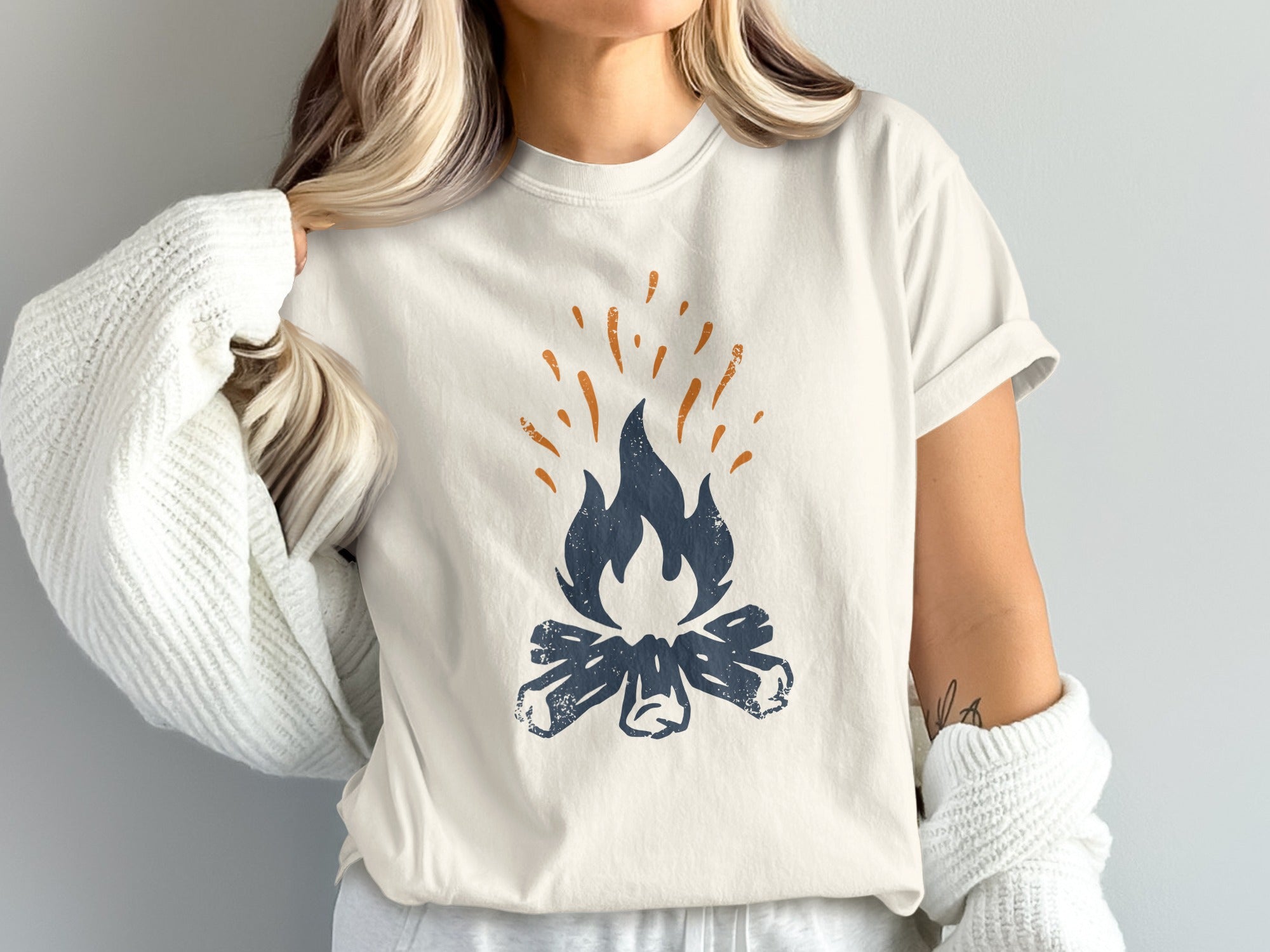 Cream t-shirt with a navy blue campfire graphic and orange sparks.