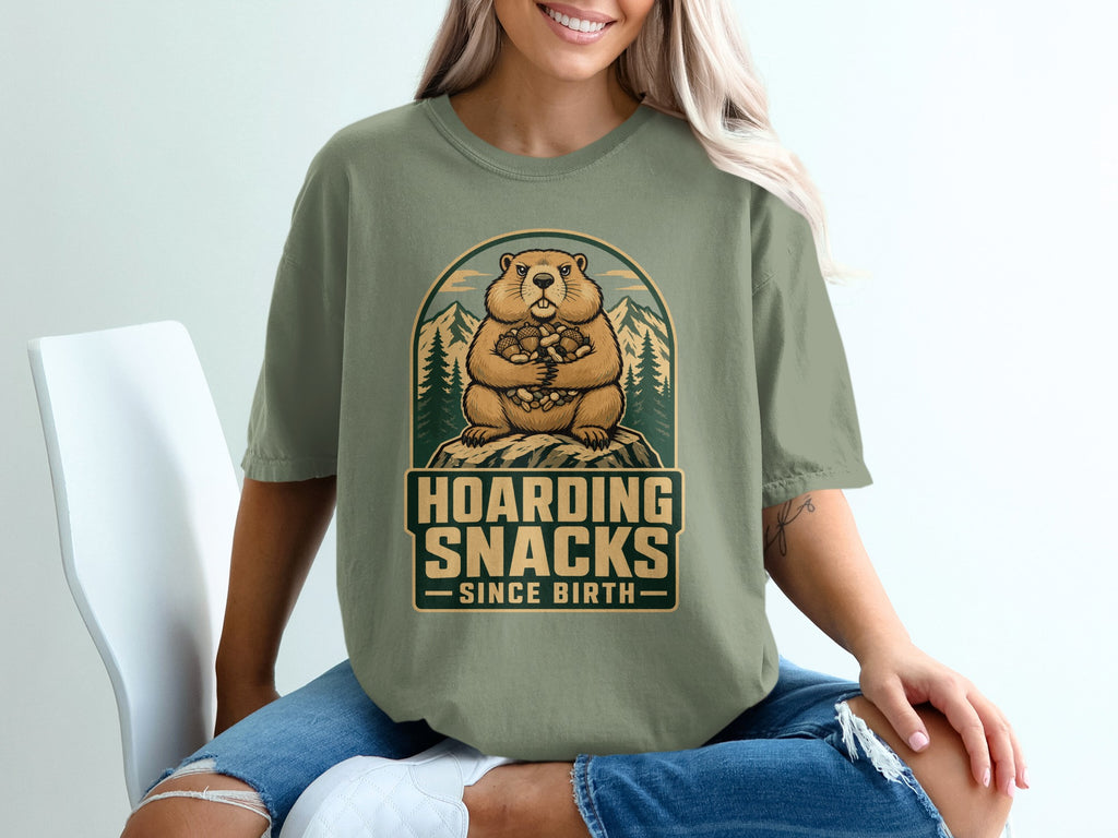 Groundhog hoarding snacks since birth graphic on a green t-shirt with mountains.