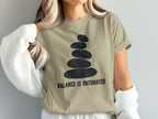 Tan t-shirt with stacked stones graphic and "BALANCE IS OVERRATED" text.