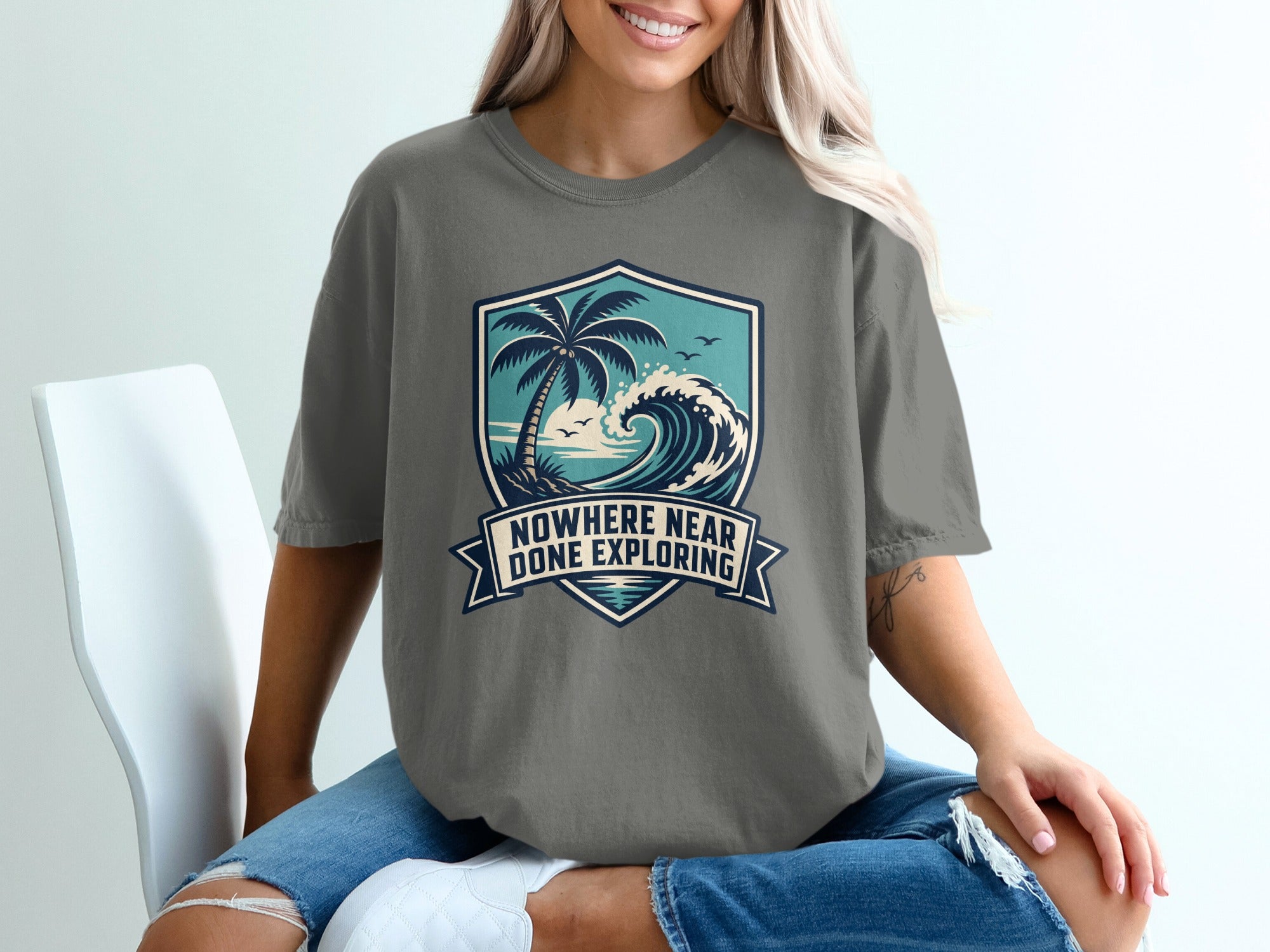 Grey t-shirt with a shield graphic of a palm tree, ocean, and text "Nowhere Near Done Exploring".