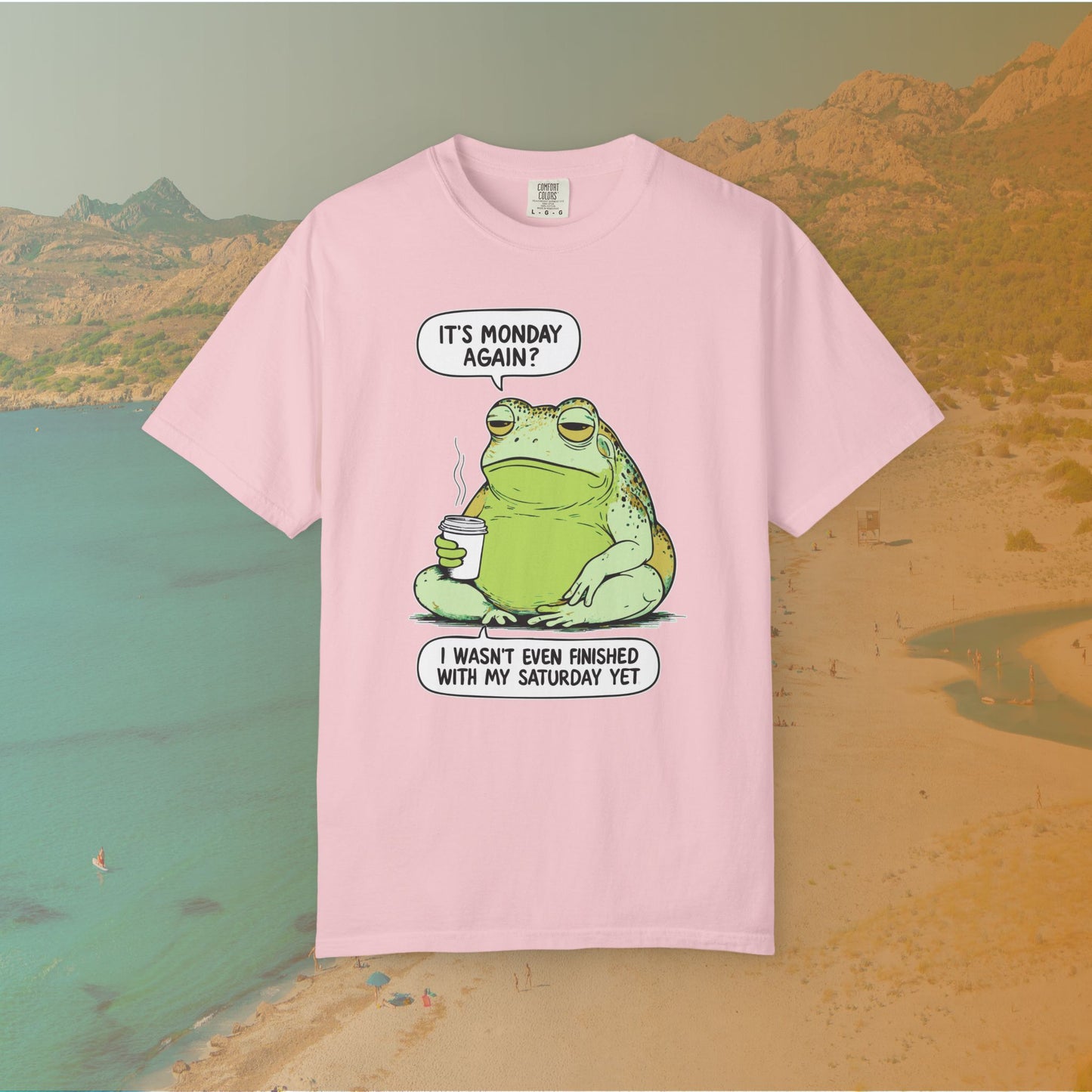 Pink T-shirt Funny T-shirt graphic featuring a large, grumpy toad holding a to-go coffee cup. The cartoon is captioned with the quotes: "IT'S MONDAY AGAIN? I WASN'T EVEN FINISHED WITH MY SATURDAY YET.