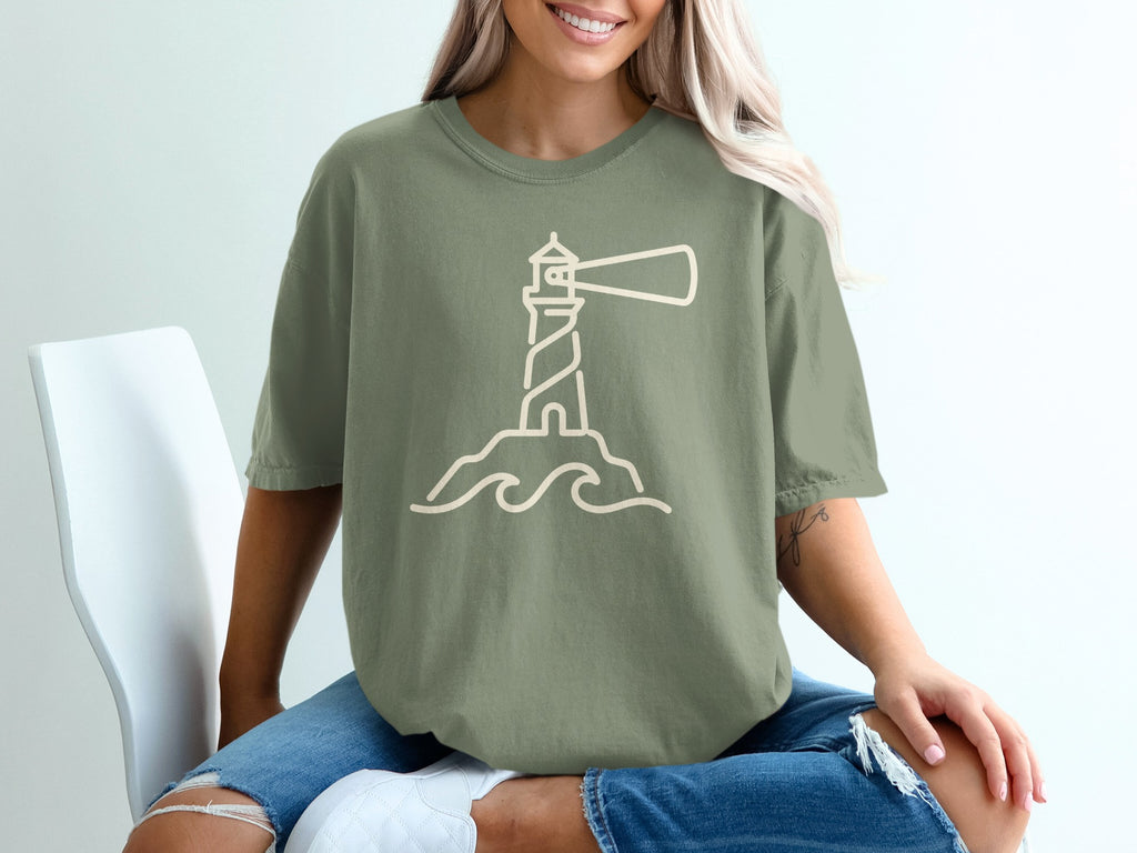 Olive green t-shirt with a beige line art lighthouse on rocks and waves.