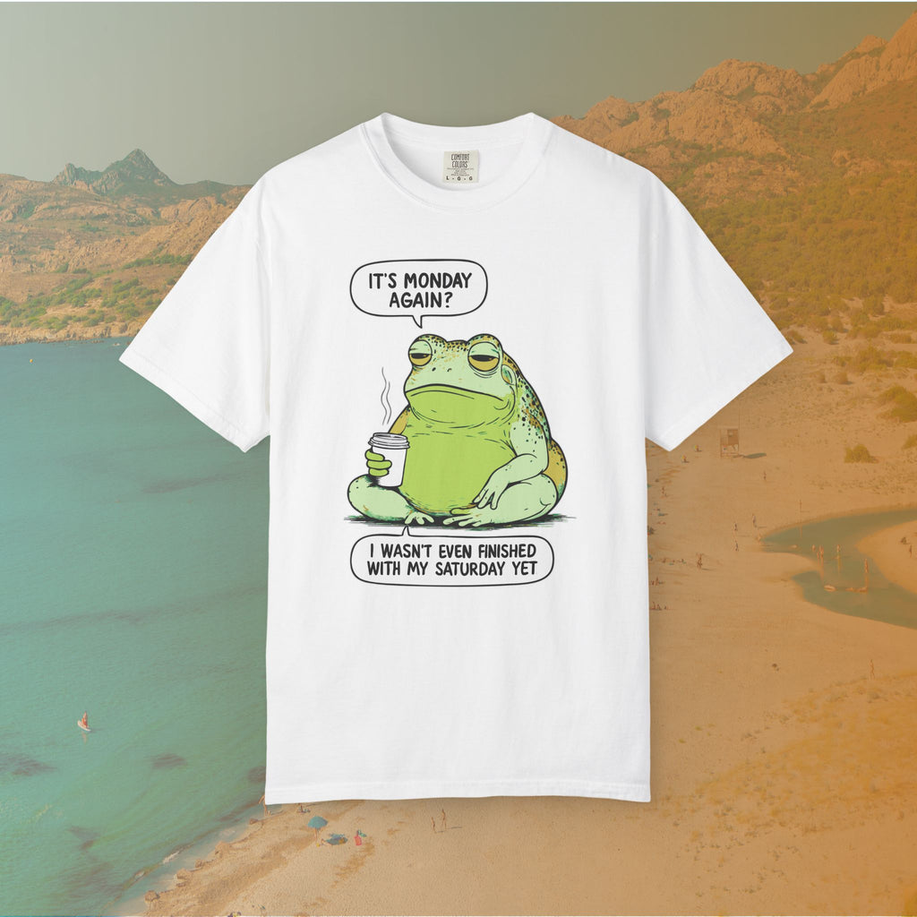 Funny T-shirt graphic featuring a large, grumpy toad holding a to-go coffee cup. The cartoon is captioned with the quotes: "IT'S MONDAY AGAIN? I WASN'T EVEN FINISHED WITH MY SATURDAY YET.
