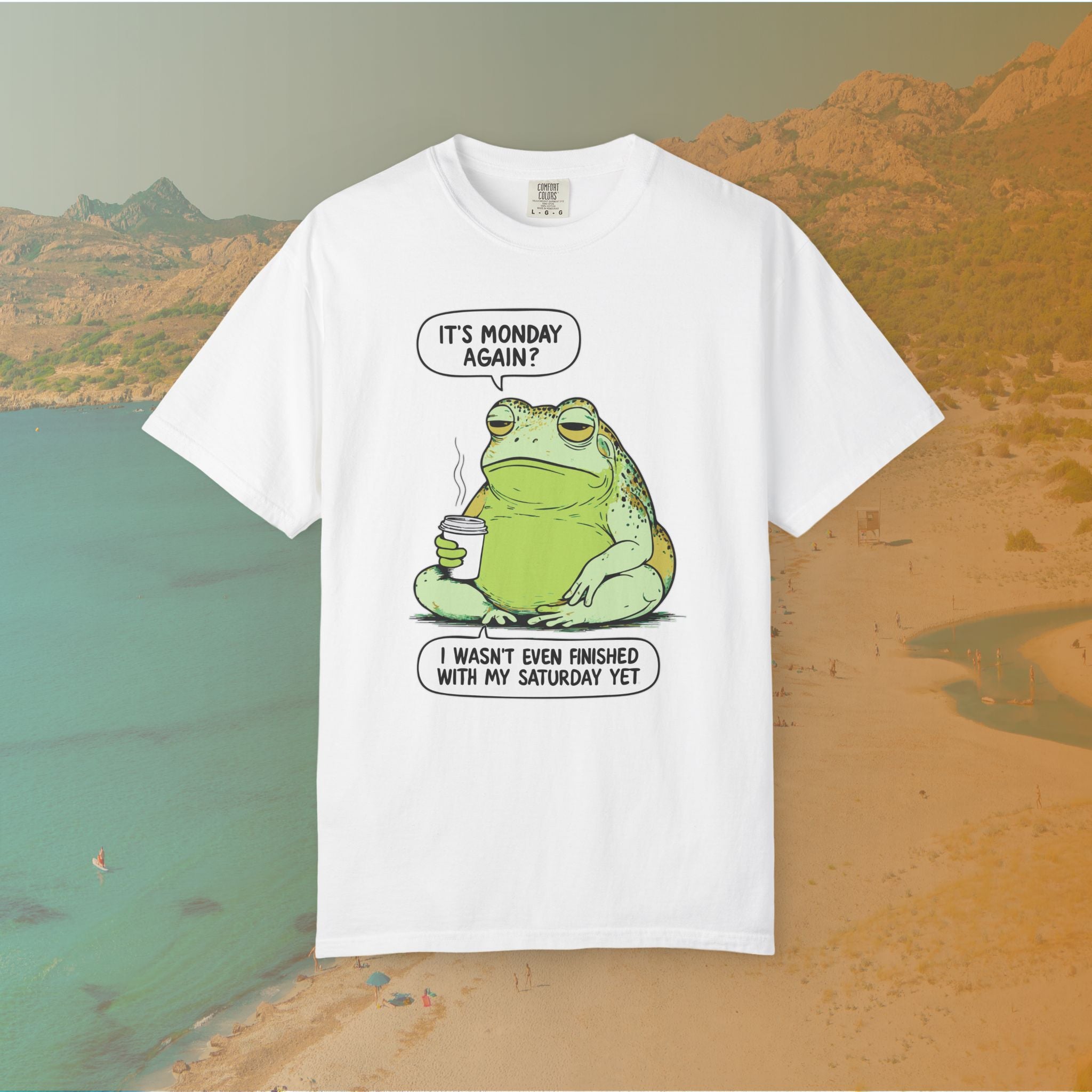 Funny T-shirt graphic featuring a large, grumpy toad holding a to-go coffee cup. The cartoon is captioned with the quotes: "IT'S MONDAY AGAIN? I WASN'T EVEN FINISHED WITH MY SATURDAY YET.
