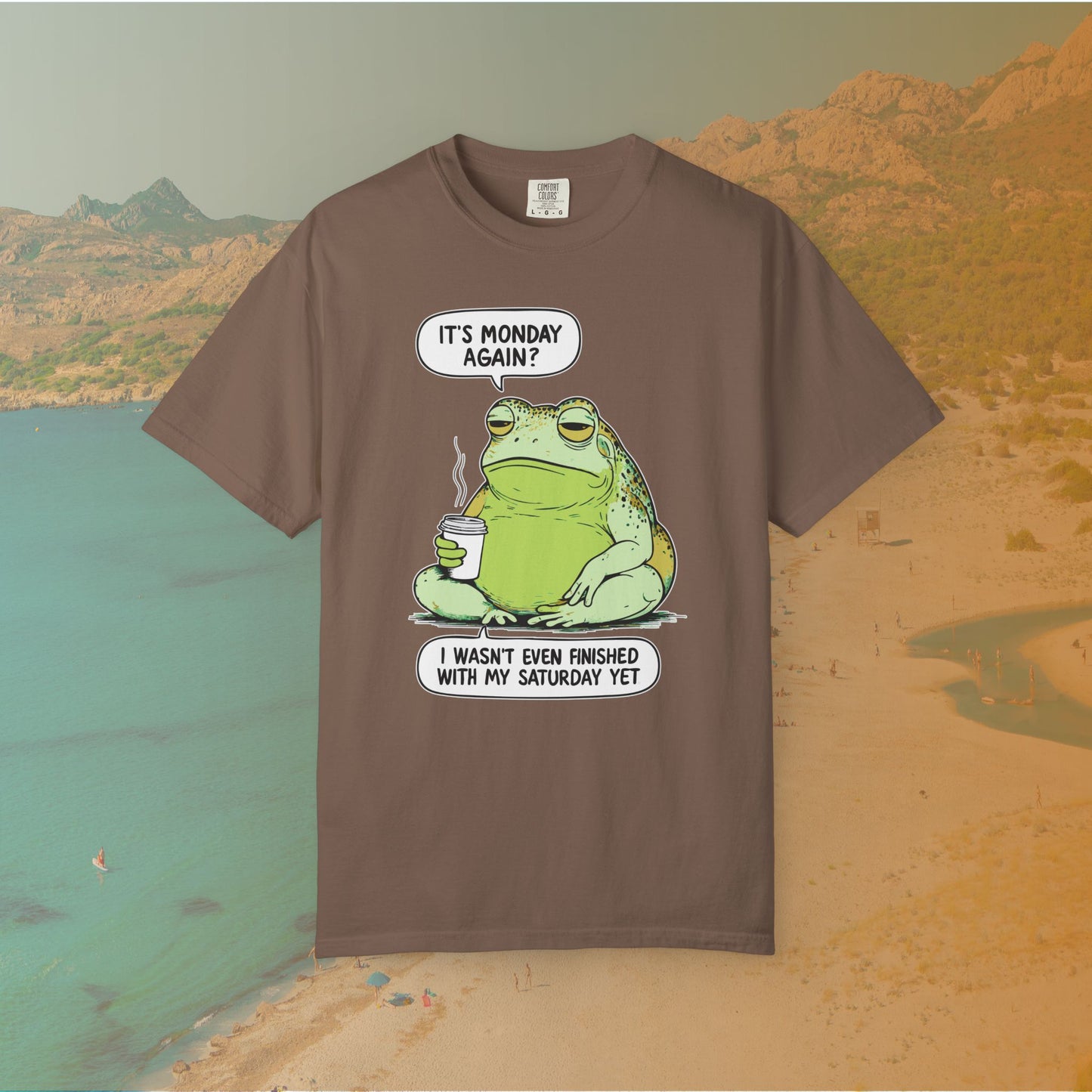 Brown T-shirt Funny T-shirt graphic featuring a large, grumpy toad holding a to-go coffee cup. The cartoon is captioned with the quotes: "IT'S MONDAY AGAIN? I WASN'T EVEN FINISHED WITH MY SATURDAY YET.
