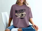 Purple t-shirt with "WILDERNESS EXPERT" text and beach scene graphic.