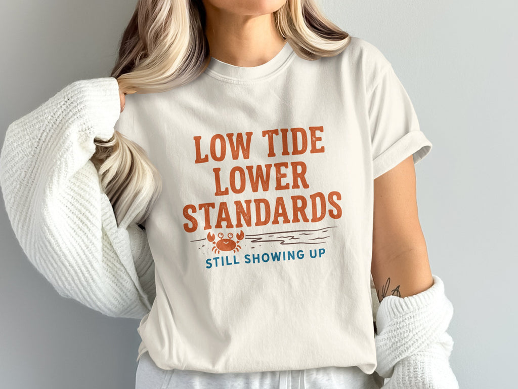 Cream t-shirt with "Low Tide, Lower Standards. Still Showing Up." text and crab graphic.