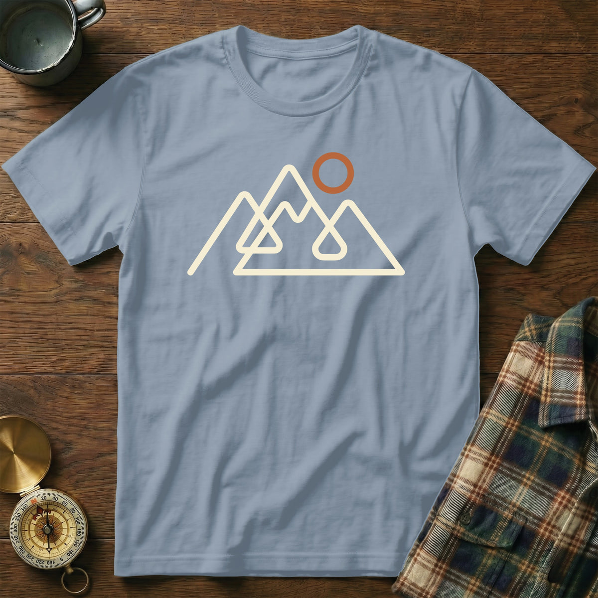 Light blue t-shirt with a cream outline of mountains and an orange sun graphic.