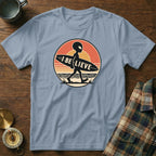 Alien carrying surfboard with "I BELIEVE" text on distressed circular background.