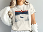 T-shirt with graphic of solo canoe on lake with mountains and sun.