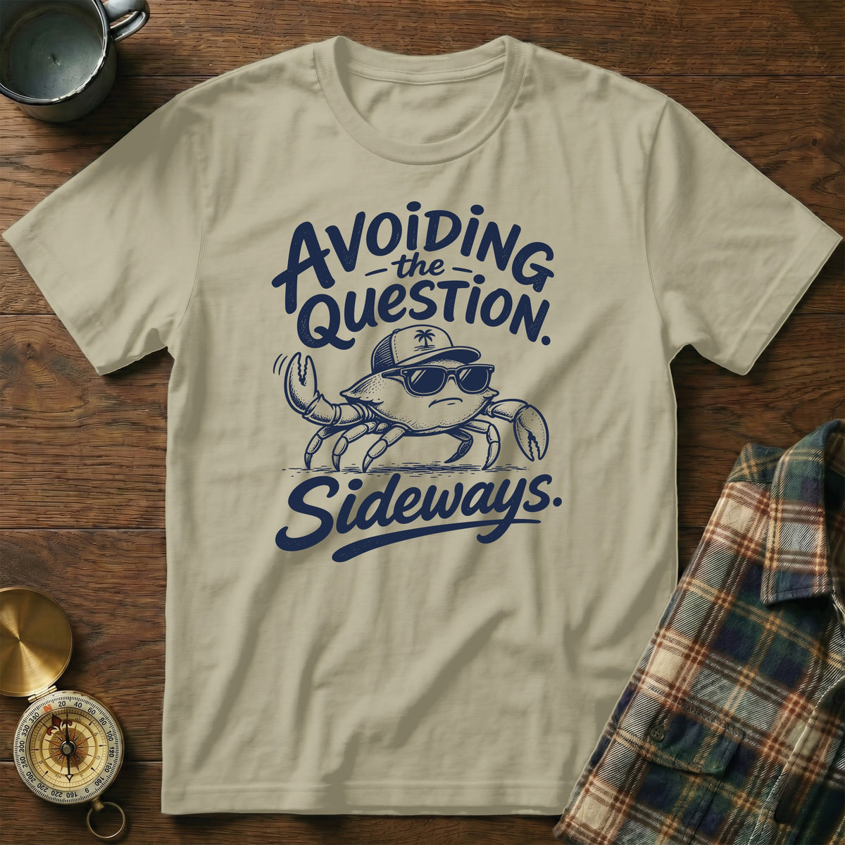 Sand-colored crewneck t-shirt featuring dark blue text that reads Avoiding the Question Sideways surrounding a cool crab wearing sunglasses.