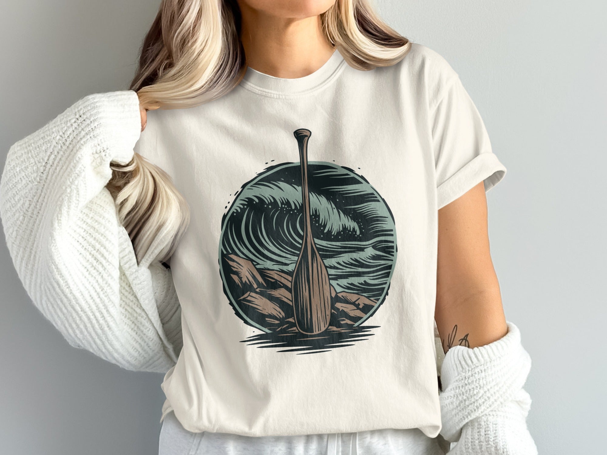 T-shirt with a circular graphic of a wooden paddle against crashing waves and rocks.